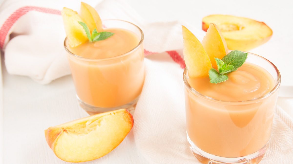 Zwei Gläser mit dem Pfirsich-Smoothie und Zitronenmelisse auf einem weiß-roten Tuch.