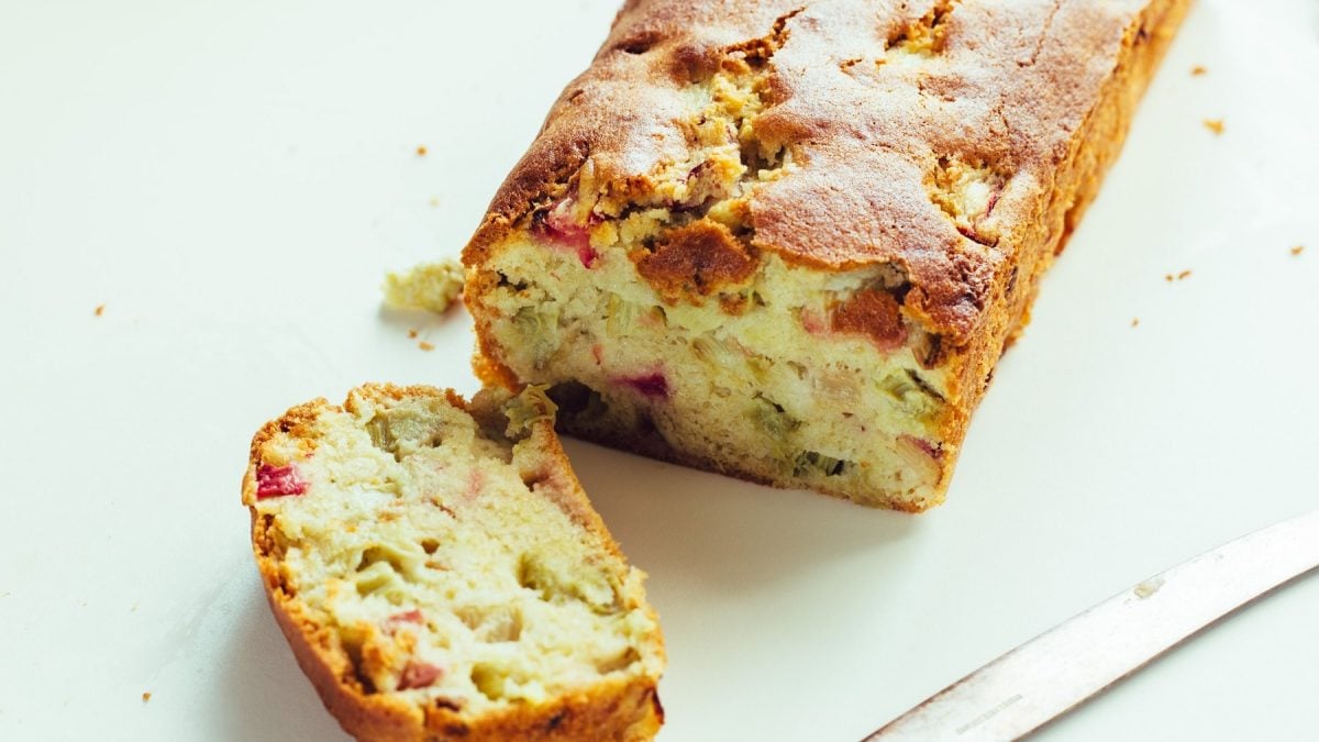 Ein Stück vom Rhabarber-Kastenkuchen udn der Rest davon auf einem hellen Untergrund.