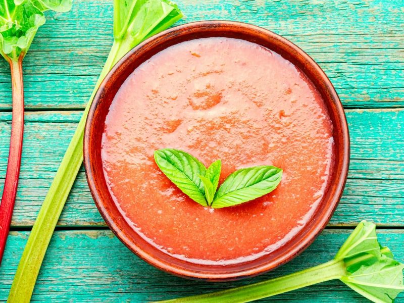 Eine rote Schüssel mit Rhabarber Smoothie Bowl auf eine türkischen Holztisch.