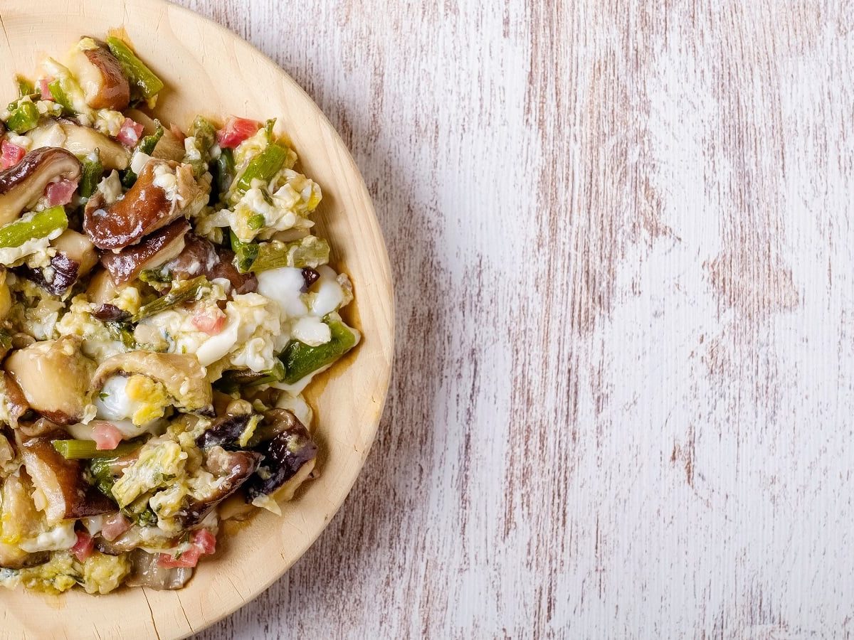 Ein Holztekker mit Spargel-Rührei mit Speck.