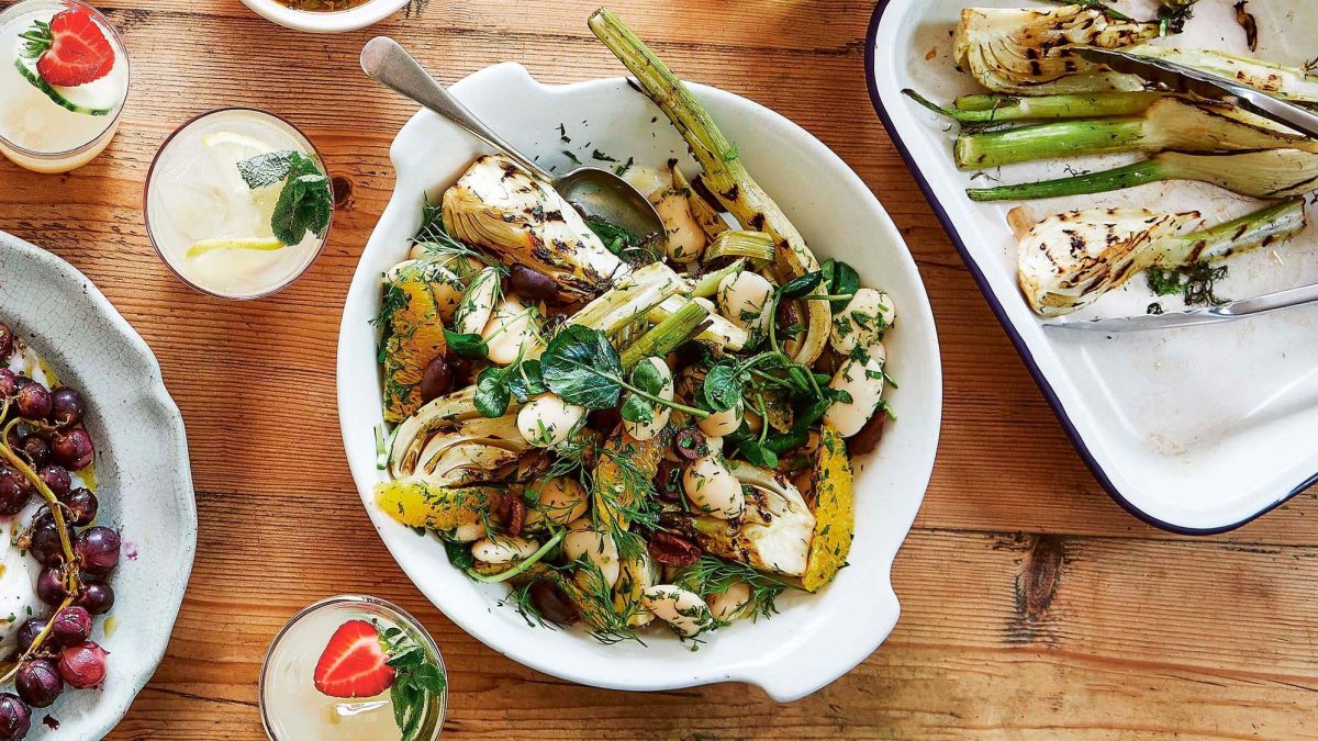 Salat mit gegrilltem Fenchel, Orange und Dill in einer Schüssel in der Draufsicht, daneben eine Auflaufform mit gerilltem Fenchel und Getränkegläser.