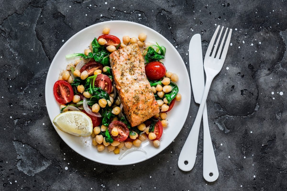 Ein runder Teller mit Kichererbsensalat mit Lachs und Spinat.