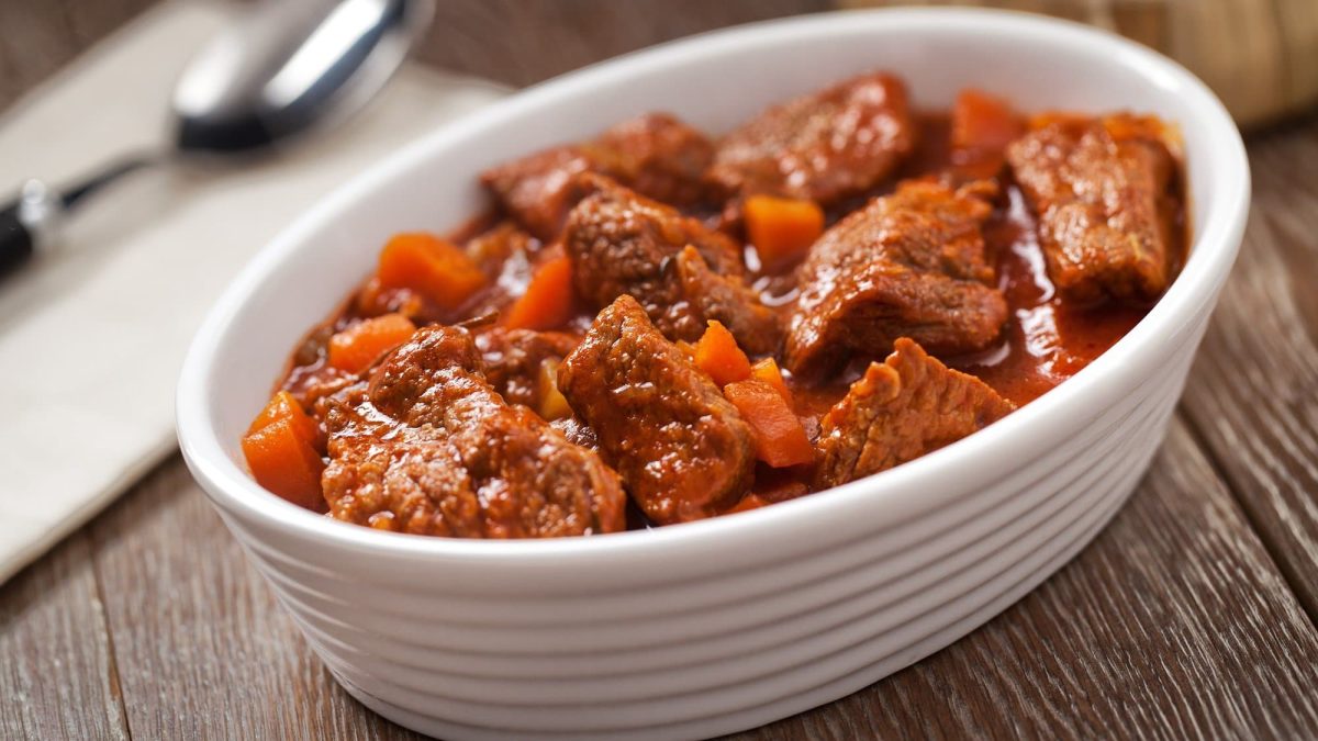 Draufsicht, schrag: eine weiße ovale Auflaufform mit Spezzatino di manzo. Dabei handelt es sich um eine italienisches Schmorgericht mit Rindfleisch.