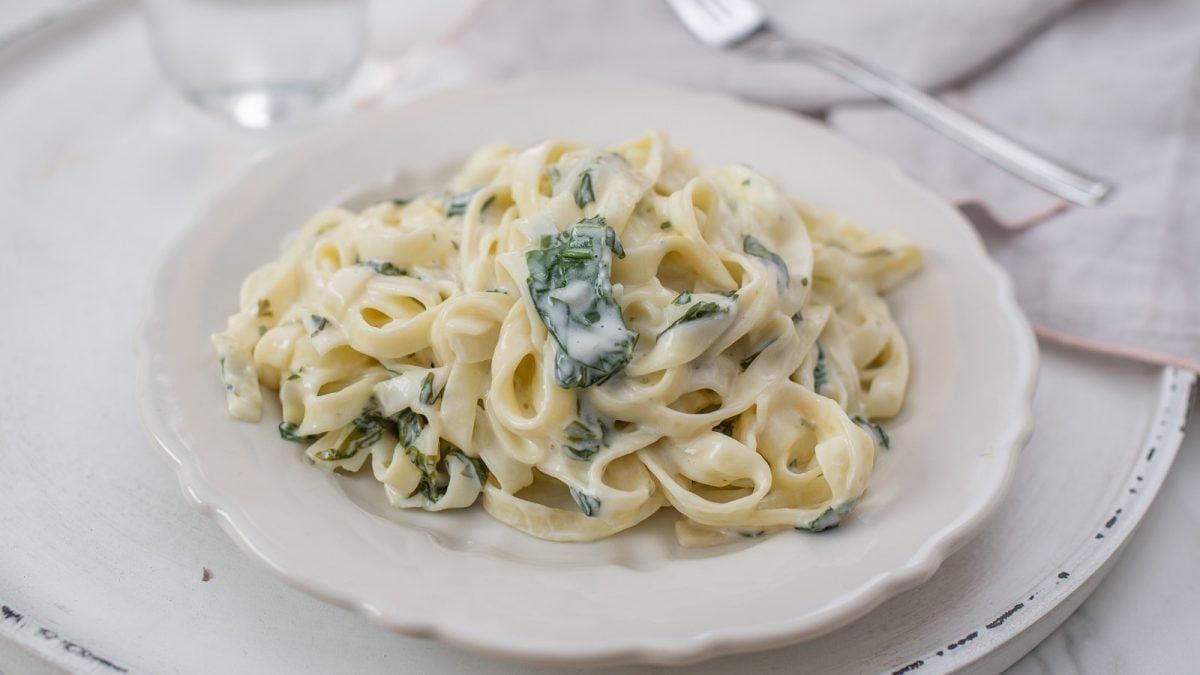 Ein weißer Pastateller mit Tagliatelle mit Bärlauchsahnesauce auf einem weißen Tisch.