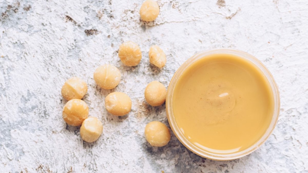 Ein Glas mit Vanille-Macadamia-Butter neben Macadamia-Nüssen.