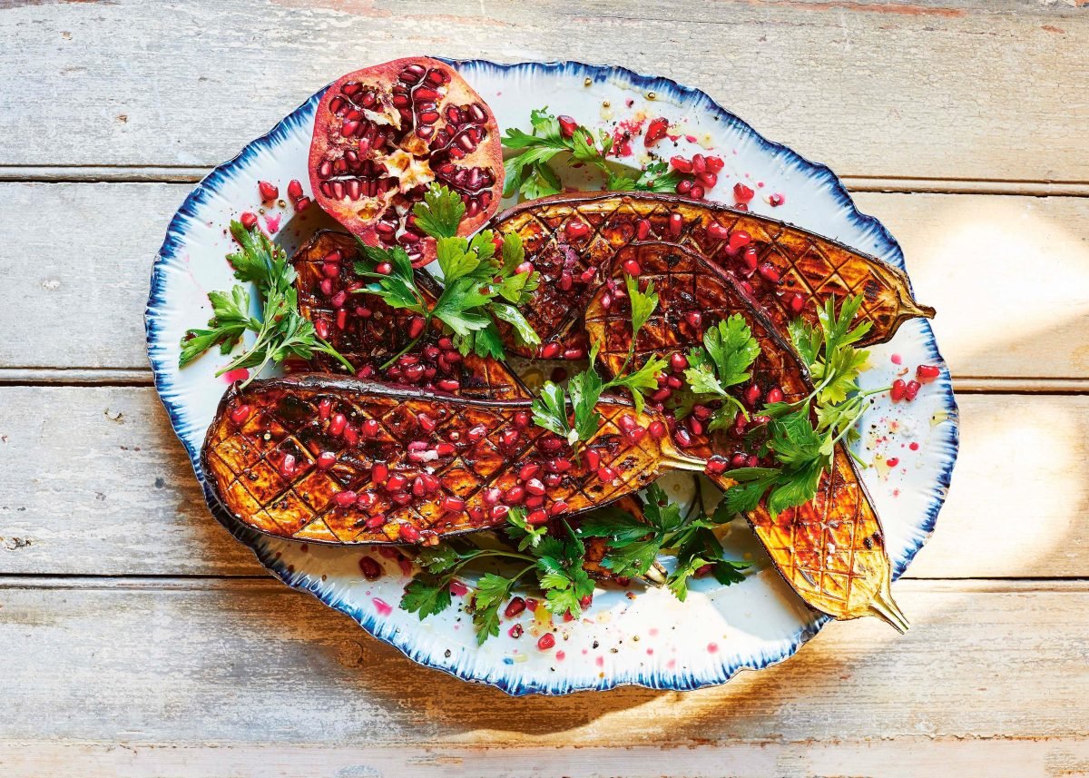 Vegan vom Grill: gegrillte Aubergine mit Tamarinde, Granatapfelkernen und frischer Petersilie auf einem Teller in der Draufsicht.