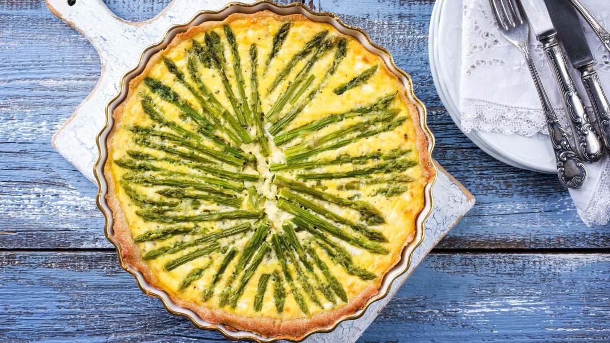 Eine vegane Spargel-Quiche in der Draufsicht, daneben Teller und Besteck.