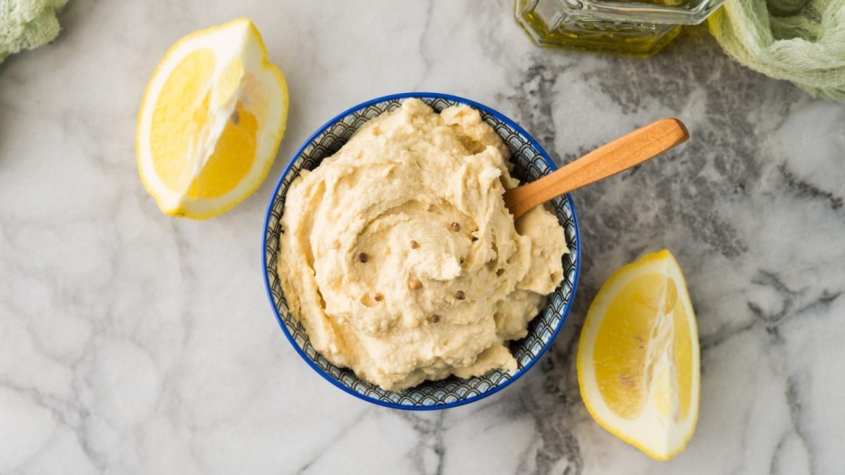 Eine blaue Schüssel mit Zitronen-Hummus auf einem Marmortisch.