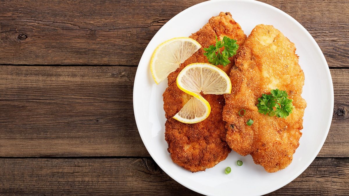 Draufsicht: Ein Teller mit zwei Brezen-Schnitzeln steht auf einem Holztisch.