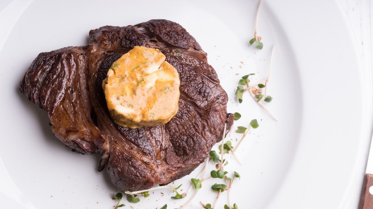Ein weißer Teller mit einem Stück Steak und Café de Paris Butter.