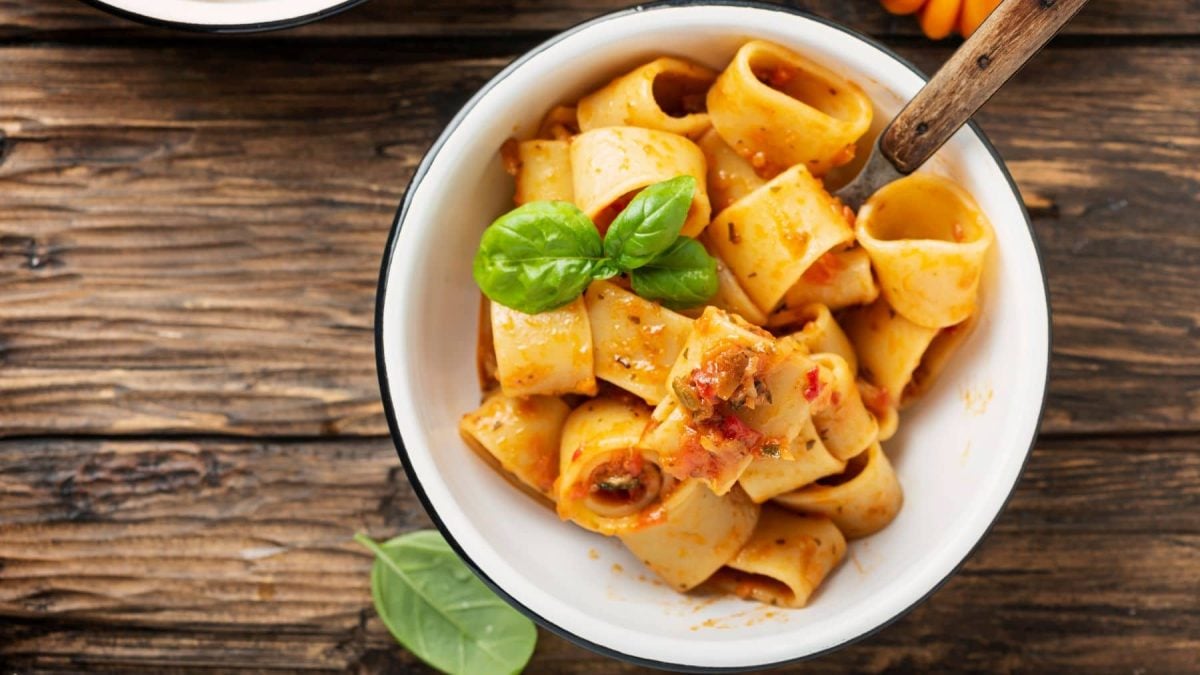 Pasta Calamarata alle Salsicce in weißem Teller mit Basilikum auf Holz. Draufsicht.