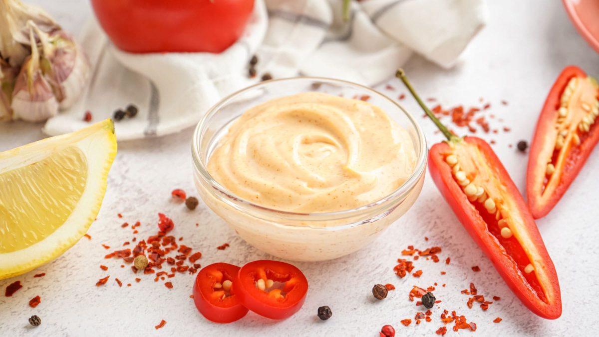 Chipotle Sauce in Glasschale mit Chilis, Gewürzen, Zitrone, Knoblauch und Tomaten auf hellem Untergrund. Drafsicht.