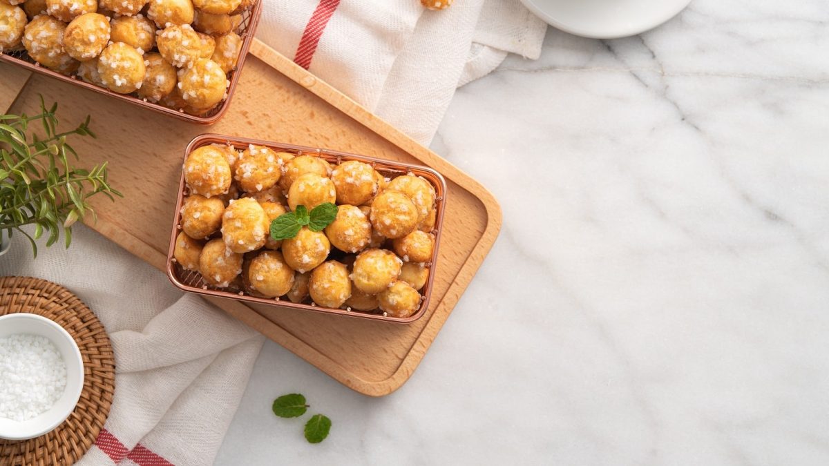 Ein Holzbrett mit Chouquettes auf einem hellen Tisch.