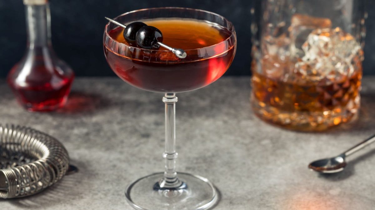 De La Louisiane Cocktail auf grauem Untergrund. Im Bild Cocktailzubehör und Gläser. Frontalansicht.