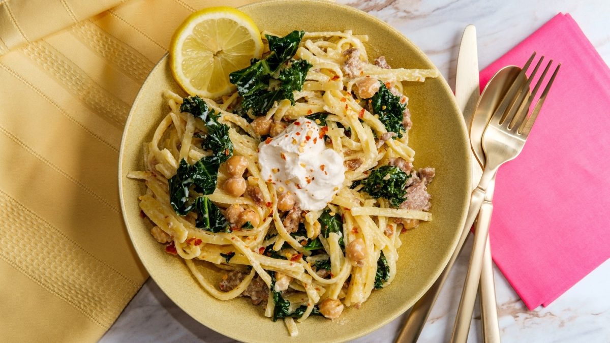 Ein gelber Teller mit Kichererbsen-Pasta mit Salsiccia und Ricotta auf einem weißen Tisch.