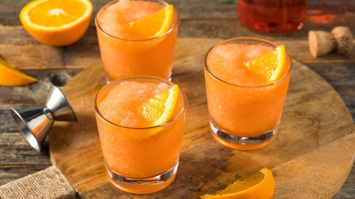 Frozen Aperol Spritz in drei Gläsern auf Holzbrett.