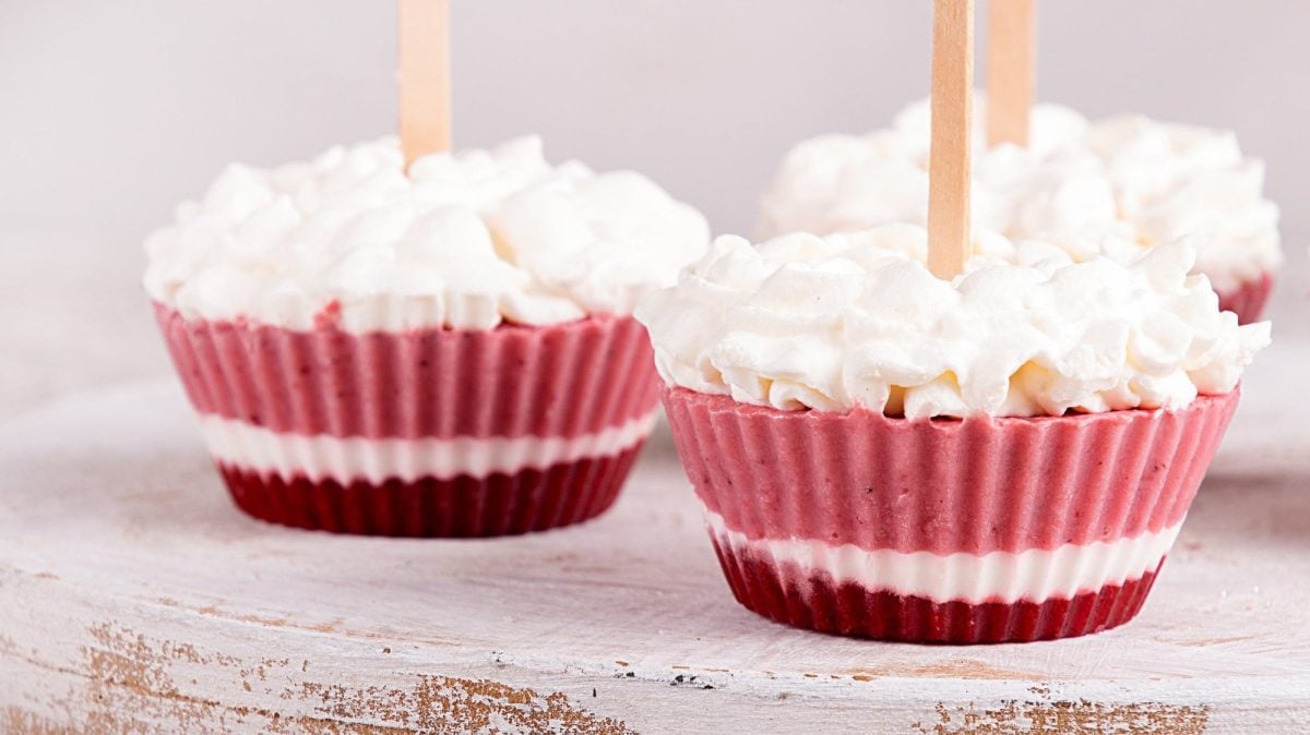 3 Frozen-Yogurt-Muffins mit Schlagsahne auf einem runden Brett.