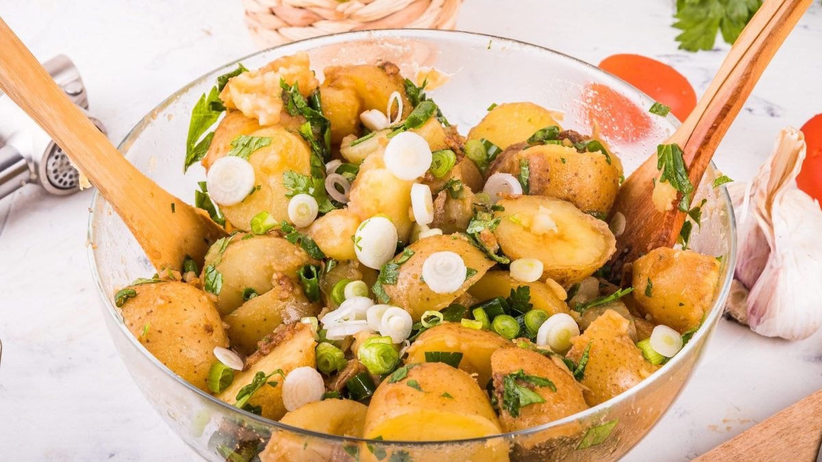 Eine Harissa-Kartoffelsalat mit Frühlingszwiebeln, darin auch Salatbesteck aus Holz.