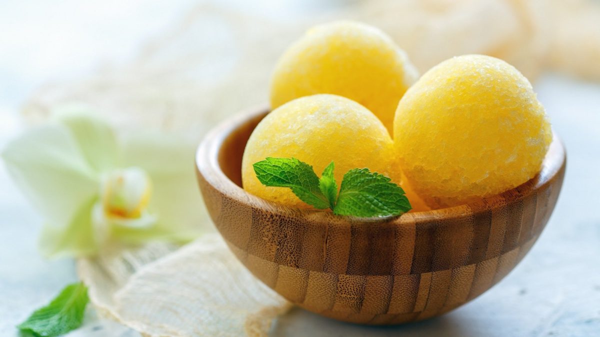 Eine Holzschale Honigmelonen-Sorbet mit 3 Kugeln und einem Zweig Minze.