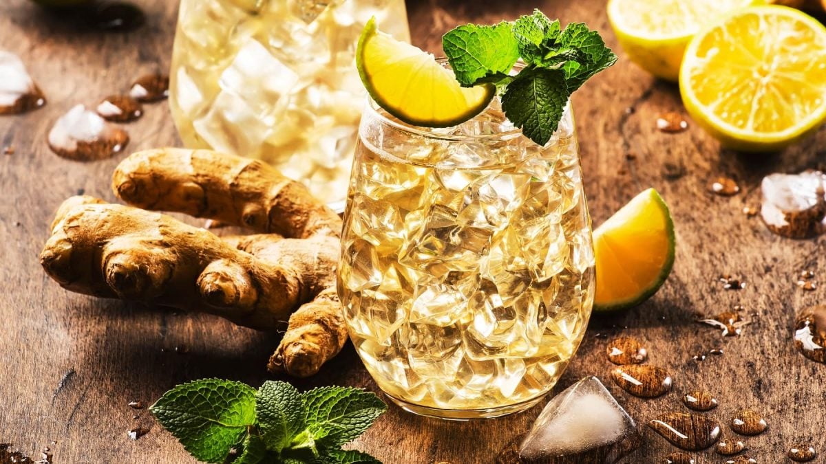 Zwei Gläser mit dem Lillet Buck auf einem Holztisch. Drum herum geschmolzenes Eis, Minze und Limette.
