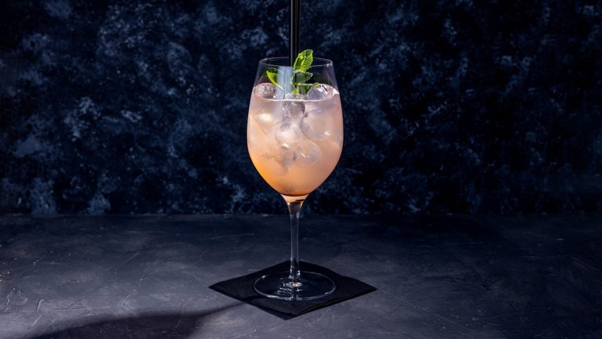 Ein Glas mit dem Cocktail auf einer schwarzen Serviette vor einem dunkelblauen Unter- und Hintergrund.