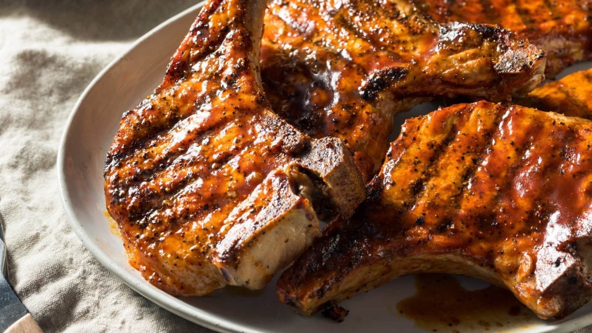 Marinierte Schweinekoteletts vom Grill auf weißem Teller und hellem Untergrund. Draufsicht.