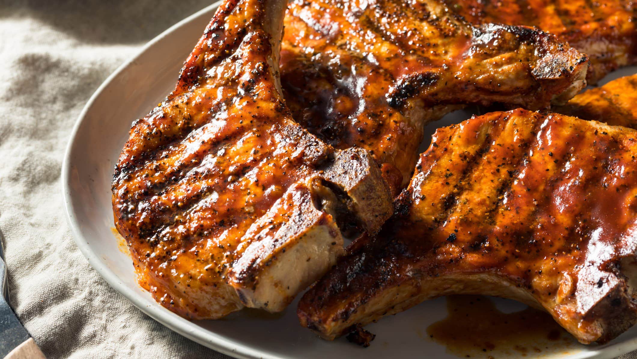 Marinierte Schweinekoteletts vom Grill auf weißem Teller und hellem Untergrund. Draufsicht.