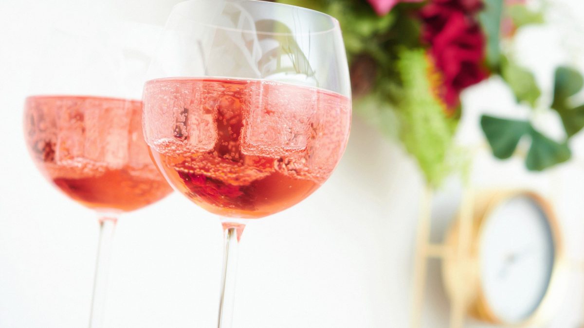 Zwei Martini Fiero Rosé Spritz in Weingläsern vor hellem Hintergrund mit floraler Deko. Frontalansicht.