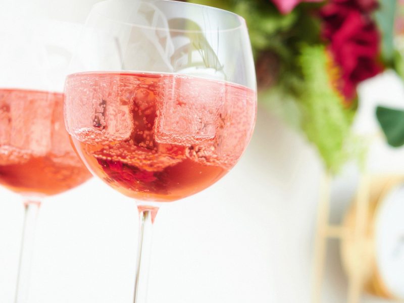 Zwei Martini Fiero Rosé Spritz in Weingläsern vor hellem Hintergrund mit floraler Deko. Frontalansicht.