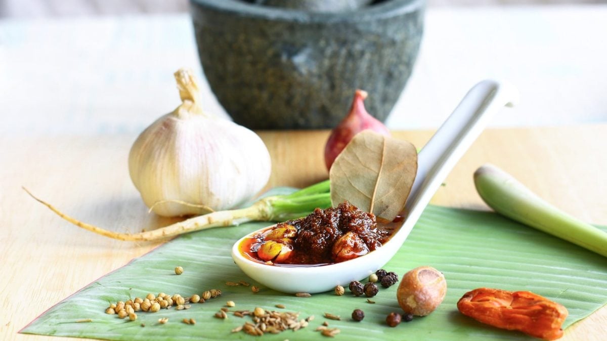 Ein Löffel mit Massaman Currypaste neben Gewürzen auf einem Bananenblatt.