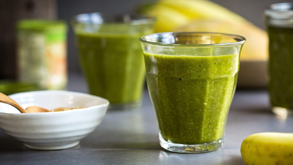 Ein Glas mit Matcha Mango Smoothie auf einem grauen Tisch
