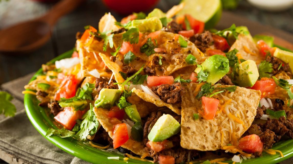 Ein grüner Teller mit dem Nacho-Salat auf einem Holztisch.