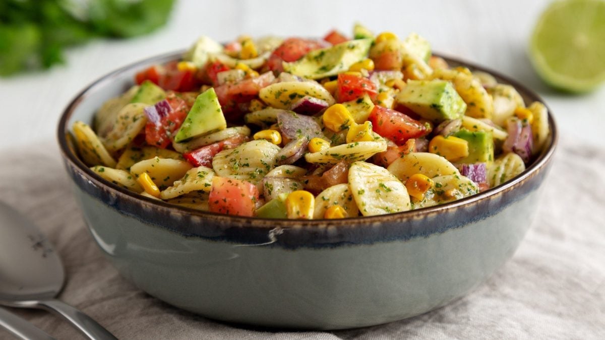 Eine Schüssel Nudelsalat mit Mais und Avocado sowie Paprika auf weißem Untergrund.