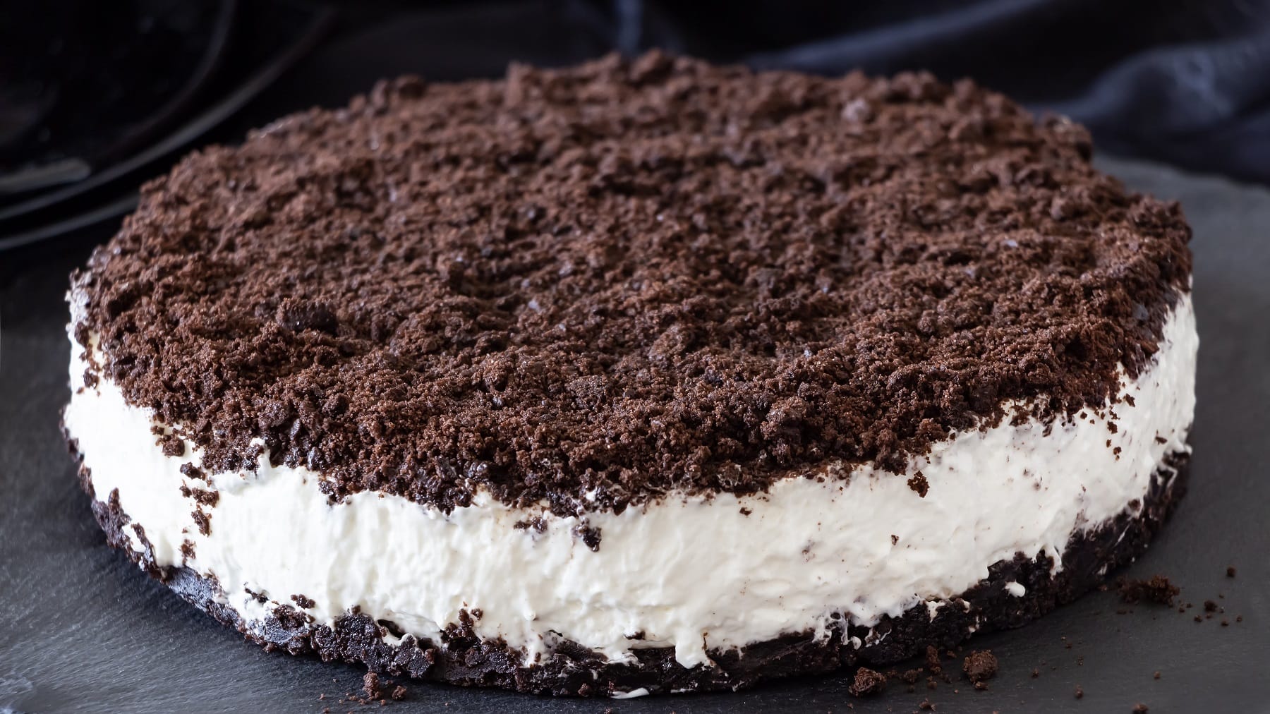 Die Oreo-Torte auf einer schwarzen Schieferplatte und im Hintergrund blauer Stoff.