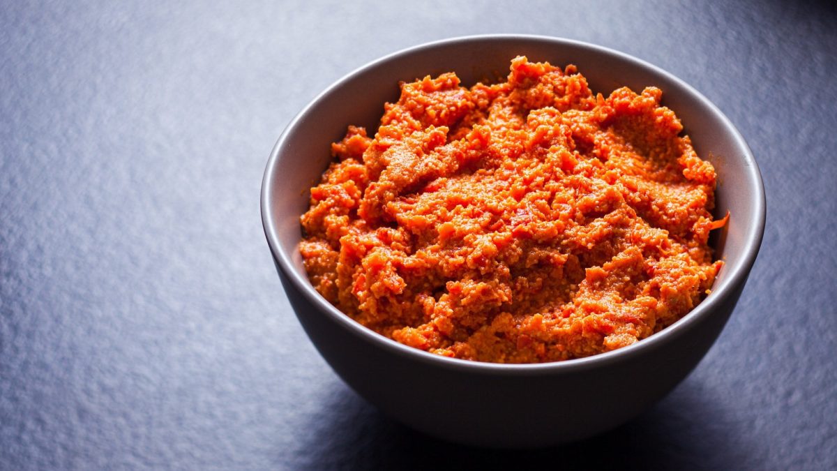 Eine dunkle Schale mit orangefarbenem Paprika-Cashew-Aufstrich.