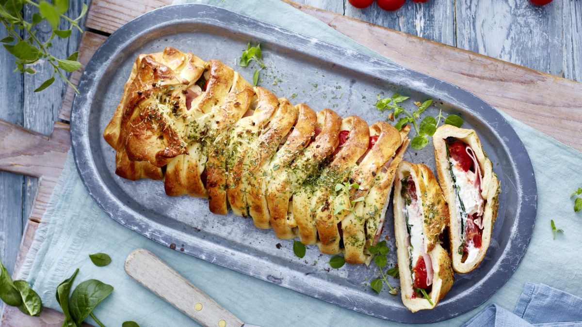 Eine Pizzarolle auf einem silbernen Servierteller auf einem hölzernen Schneidebrett mit einem hellblauen Geschirrtuch.