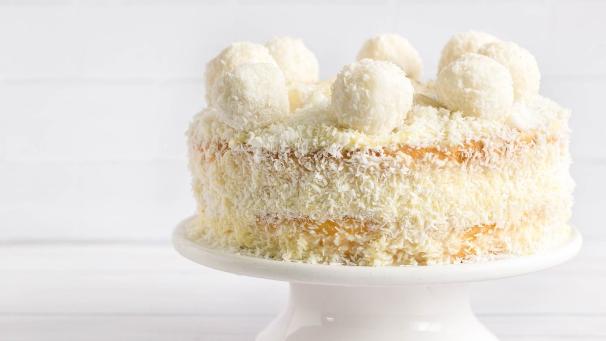 Eine Raffaello-Torte auf einem weißen Tortenständer und weißem Hinter- und Untergrund.