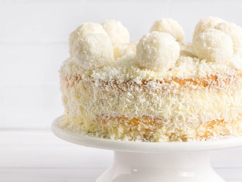 Eine Raffaello-Torte auf einem weißen Tortenständer und weißem Hinter- und Untergrund.