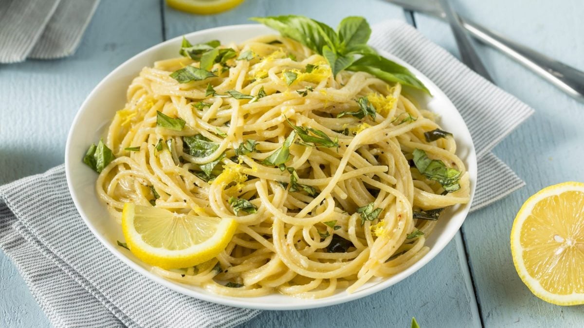 Ein weißer Teller mit der Ricotta Lemon Pasta auf einem hellen Holztisch mit grauen Tischdecken.