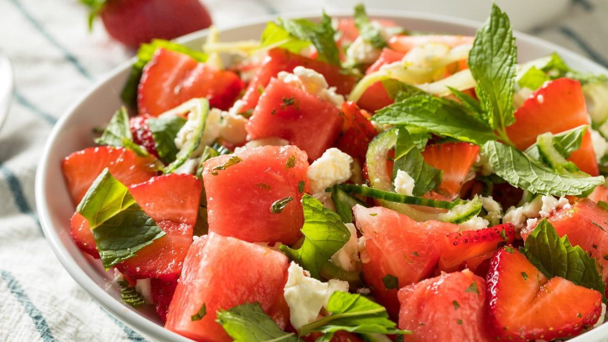 Eine weiße Schüssel mit dem Sommersalat auf einem blau-weiß-gestreiftem Tuch.