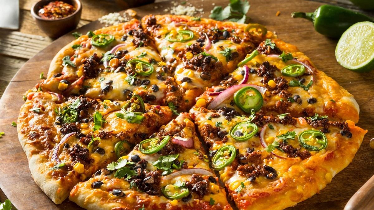Eine runde Pizza auf einem Holzbrett mit den mexikanischen Zutaten belegt.