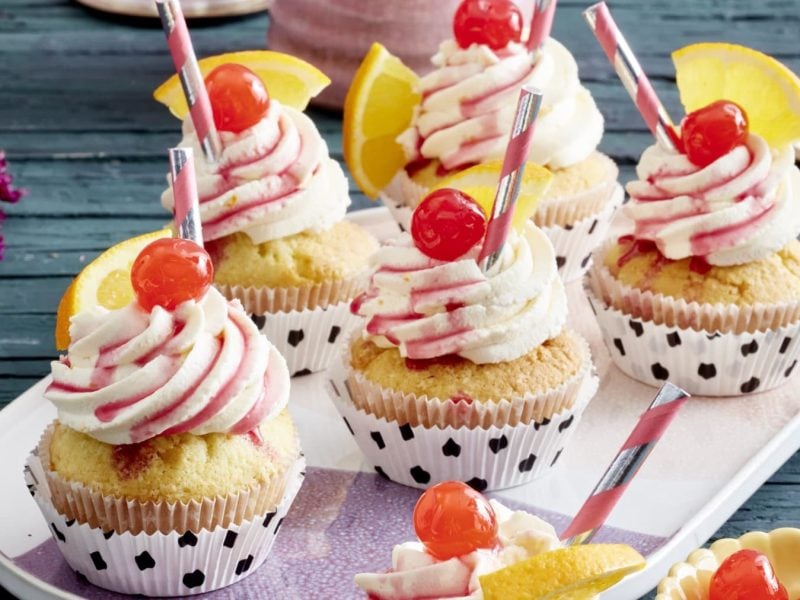 5 Stück Tequila Sunrise-Muffins auf einem hellrosa Servierteller auf einem dunkelgrau-hölzernen Tisch