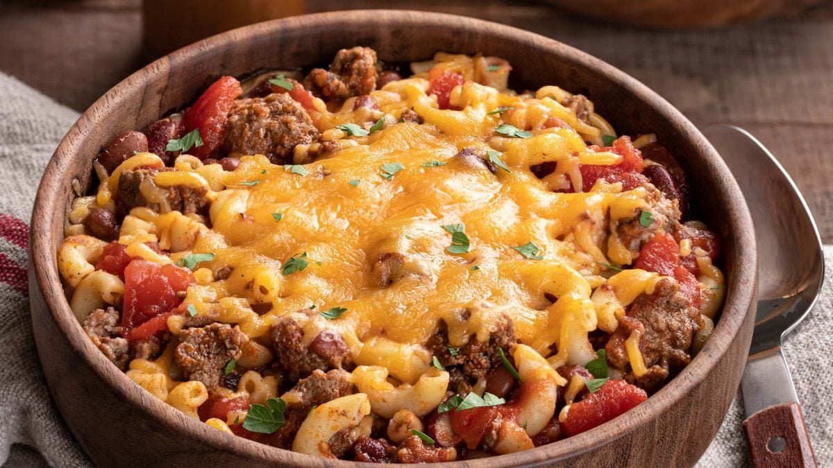 Eine braune Holzschale mit der Pasta im Tex-Mex-Style auf einem dunklen Holztisch mit Salz- und Pfefferstreuer aus Holz.