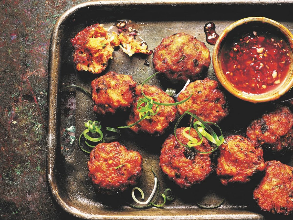 Mehrere Fischkroketten auf einem dunklen Teller mit Sweet-Chili-Sauce.