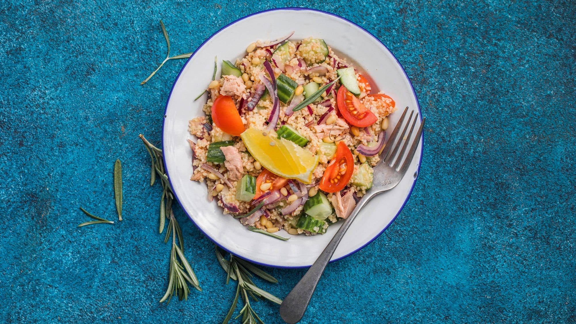 Draufsicht: auf einem blauen Untergrund steht ein weißer Teller mit einem Thunfischsalat mit Couscous.