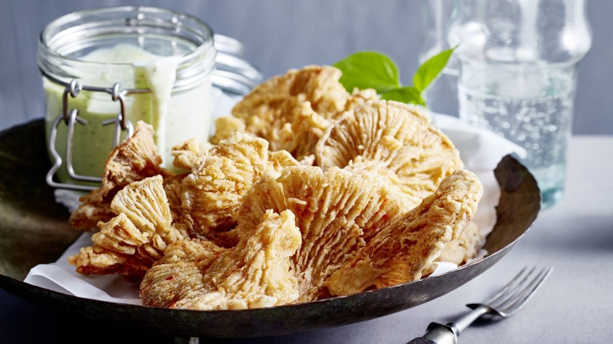 Vegane Calamari mit Tofu-Basilikum-Aioli auf einem dunklen Teller, grauer Hintergrund.