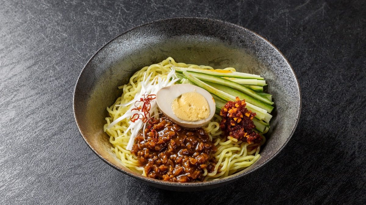 Eine Schüssel mit Zha Jiang Mian auf einem dunklen Tisch.