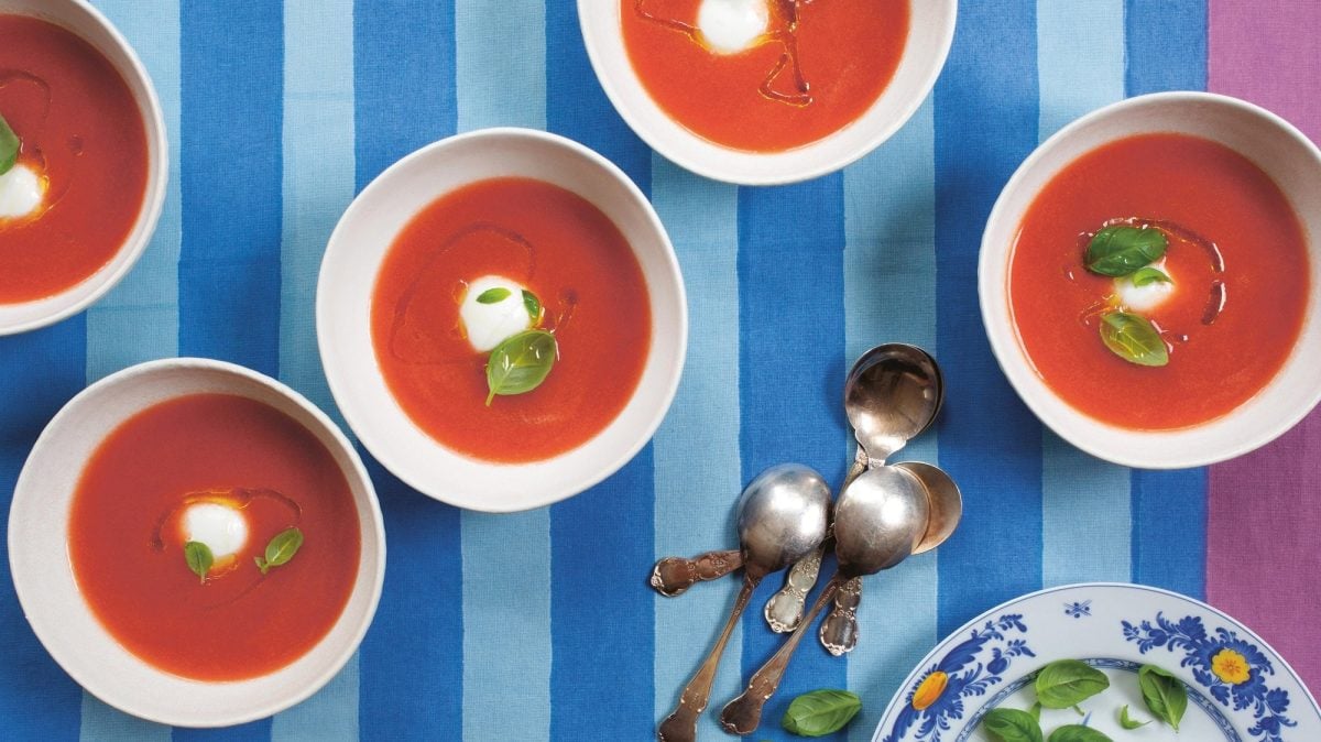 Ein paar weiße Schüsseln mit der Tomatensuppe Acgua de Pomodoro garniert mit Basilikum, Öl und Mozzarella, daneben drei Löffe, alles Draufsicht.