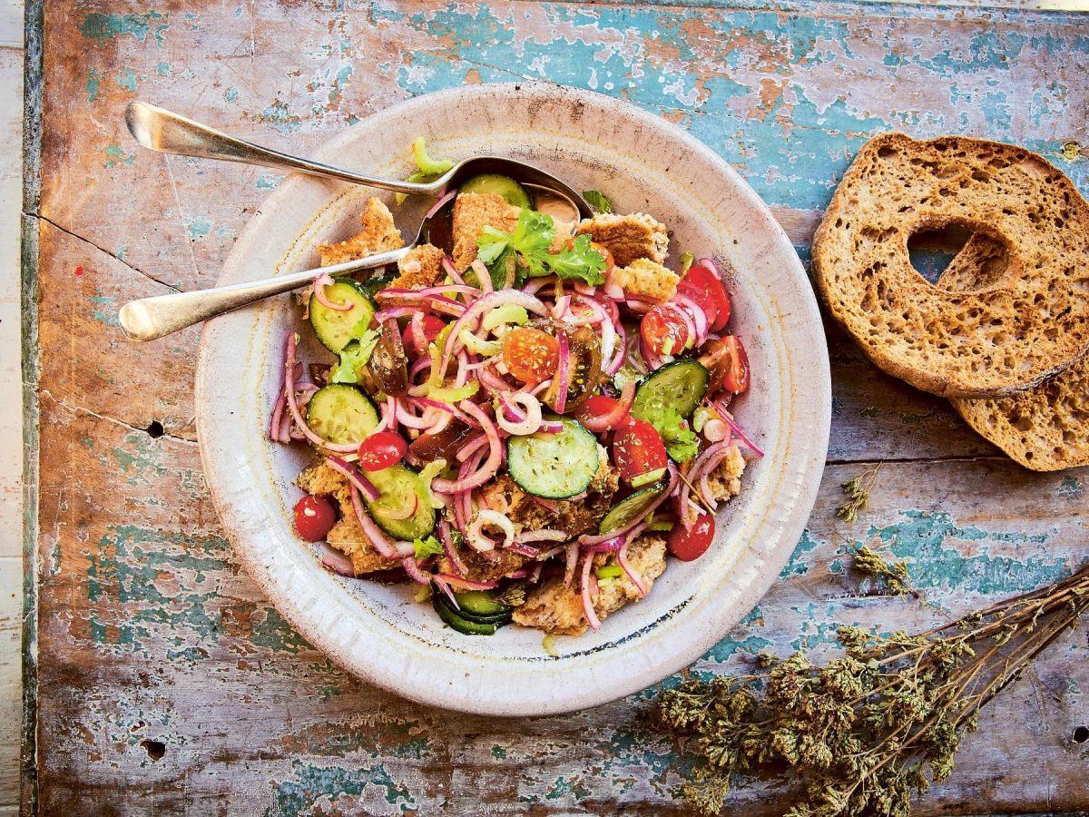 Ein weißer Teller mit dem apulischen Brotsalat auf einem rustikalen Holztisch.