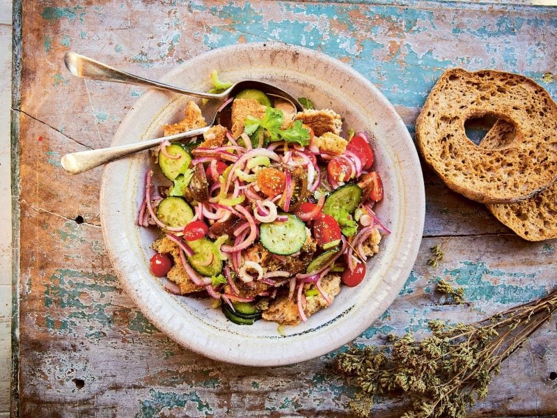 Ein weißer Teller mit dem apulischen Brotsalat auf einem rustikalen Holztisch.